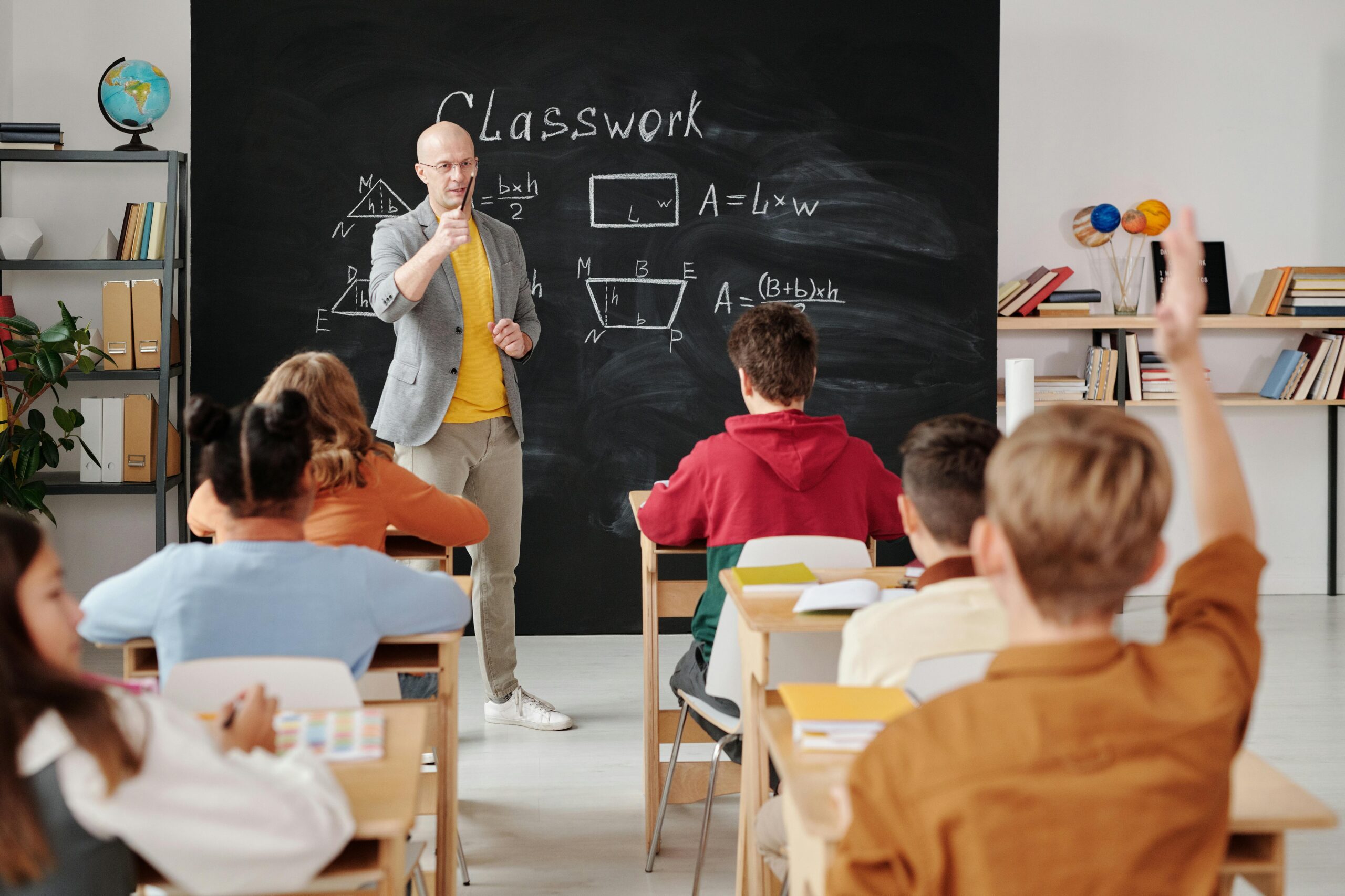 students in class; one raising hand for teacher to tell him that he has an nyc dental emergency